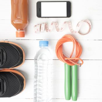 fitness equipment:running shoes,phone,measuring tape,water,juice and jumpong rope on white wood background