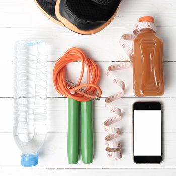 fitness equipment:running shoes,phone,measuring tape,water,juice and jumpong rope on white wood background