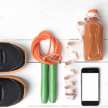 fitness equipment:running shoes,phone,measuring tape,water,juice and jumpong rope on white wood background