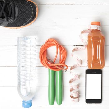 fitness equipment:running shoes,phone,measuring tape,water,juice and jumpong rope on white wood background