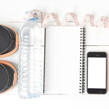 fitness equipment:running shoes,water,measuring tape,notepad,phone and juice on white wood background