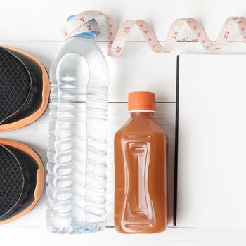 fitness equipment:running shoes,water,measuring tape,notepad,phone and juice on white wood background