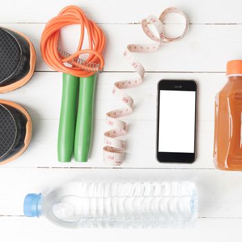 fitness equipment:running shoes,phone,measuring tape,water,juice and jumpong rope on white wood background