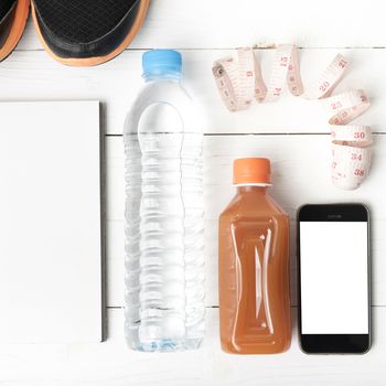 fitness equipment:running shoes,water,measuring tape,notepad,phone and juice on white wood background