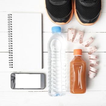 fitness equipment:running shoes,water,measuring tape,notepad,phone and juice on white wood background