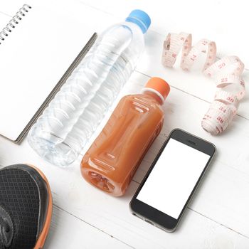 fitness equipment:running shoes,water,measuring tape,notepad,phone and juice on white wood background