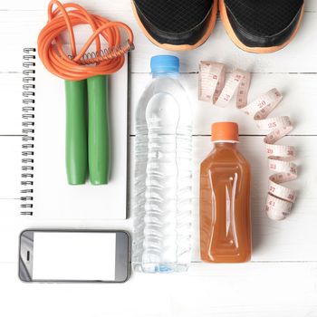 fitness equipment:running shoes,jumping rope,notepad,phone,water,juice and measuring tape on white wood background