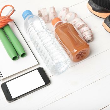 fitness equipment:running shoes,jumping rope,notepad,phone,water,juice and measuring tape on white wood background