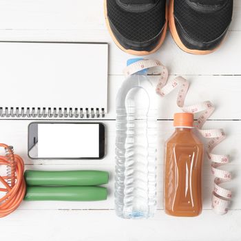 fitness equipment:running shoes,jumping rope,notepad,phone,water,juice and measuring tape on white wood background