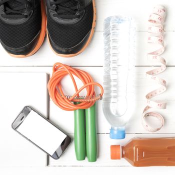 fitness equipment:running shoes,jumping rope,notepad,phone,water,juice and measuring tape on white wood background