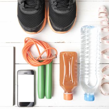 fitness equipment:running shoes,jumping rope,notepad,phone,water,juice and measuring tape on white wood background