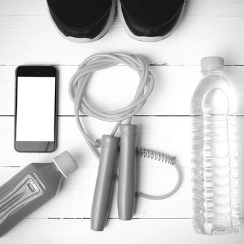 fitness equipment : running shoes,jumping rope,water,juice and phone on white wood background black and white color