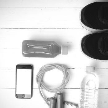 fitness equipment : running shoes,jumping rope,water,juice and phone on white wood background black and white color