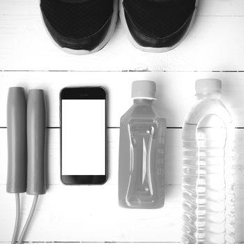 fitness equipment : running shoes,jumping rope,water,juice and phone on white wood background black and white color