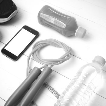 fitness equipment : running shoes,jumping rope,water,juice and phone on white wood background black and white color