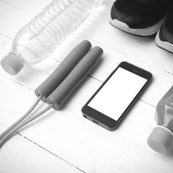 fitness equipment : running shoes,jumping rope,water,juice and phone on white wood background black and white color