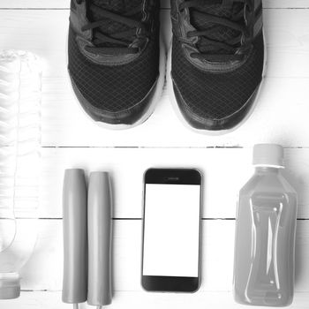 fitness equipment : running shoes,jumping rope,water,juice and phone on white wood background black and white color