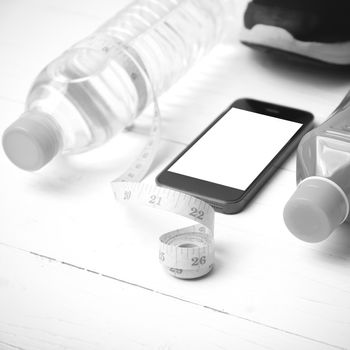 fitness equipment:running shoes,measuring tape,water,juice and phone on white wood background black and white color