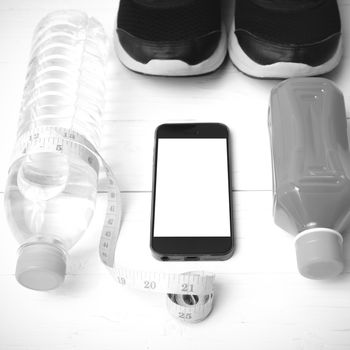 fitness equipment:running shoes,measuring tape,water,juice and phone on white wood background black and white color