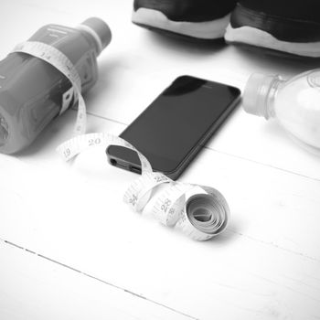 fitness equipment:running shoes,measuring tape,water,juice and phone on white wood background black and white color