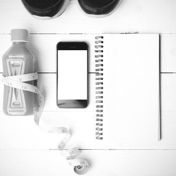 fitness equipment:running shoes,juice,measuring tape,notepad and phone on white wood background black and white color