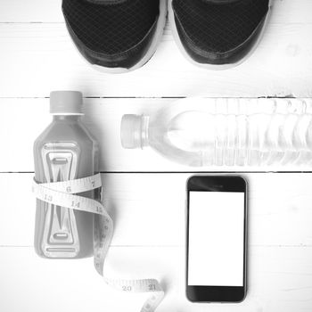 fitness equipment:running shoes,measuring tape,water,juice and phone on white wood background black and white color