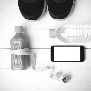 fitness equipment:running shoes,measuring tape,water,juice and phone on white wood background black and white color