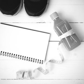 fitness equipment:running shoes,juice,measuring tape,notepad and phone on white wood background black and white color