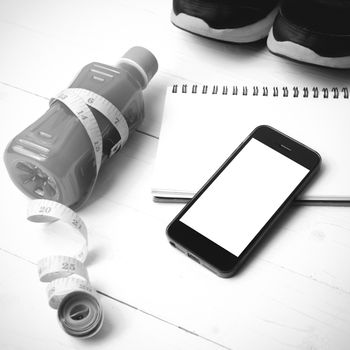 fitness equipment:running shoes,juice,measuring tape,notepad and phone on white wood background black and white color