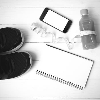 fitness equipment:running shoes,juice,measuring tape,notepad and phone on white wood background black and white color