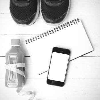 fitness equipment:running shoes,juice,measuring tape,notepad and phone on white wood background black and white color