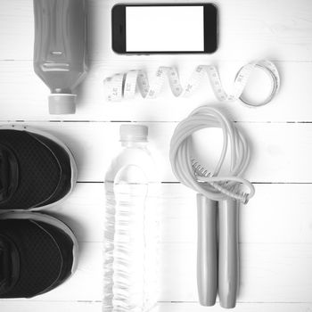 fitness equipment:running shoes,phone,measuring tape,water,juice and jumpong rope on white wood background black and white color