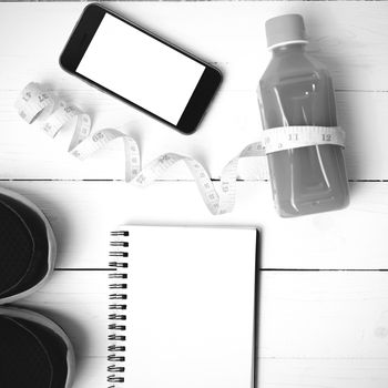 fitness equipment:running shoes,juice,measuring tape,notepad and phone on white wood background black and white color