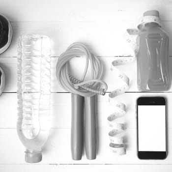 fitness equipment:running shoes,phone,measuring tape,water,juice and jumpong rope on white wood background black and white color