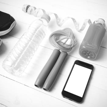 fitness equipment:running shoes,phone,measuring tape,water,juice and jumpong rope on white wood background black and white color