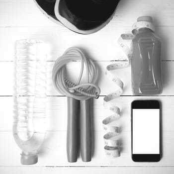 fitness equipment:running shoes,phone,measuring tape,water,juice and jumpong rope on white wood background black and white color