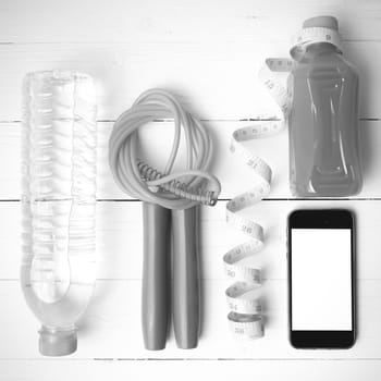 fitness equipment:running shoes,phone,measuring tape,water,juice and jumpong rope on white wood background black and white color