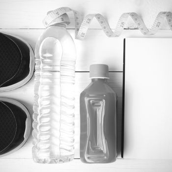 fitness equipment:running shoes,water,measuring tape,notepad,phone and juice on white wood background black and white color