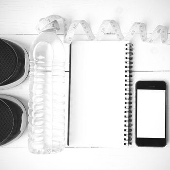 fitness equipment:running shoes,water,measuring tape,notepad,phone and juice on white wood background black and white color