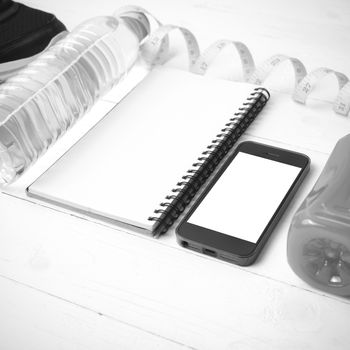 fitness equipment:running shoes,water,measuring tape,notepad,phone and juice on white wood background black and white color