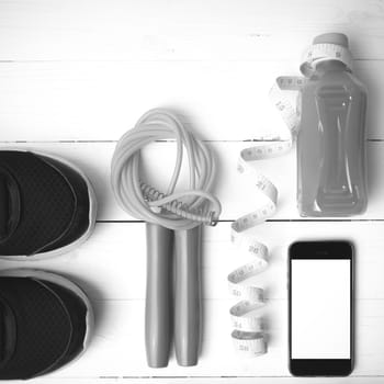 fitness equipment:running shoes,phone,measuring tape,water,juice and jumpong rope on white wood background black and white color