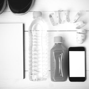 fitness equipment:running shoes,water,measuring tape,notepad,phone and juice on white wood background black and white color