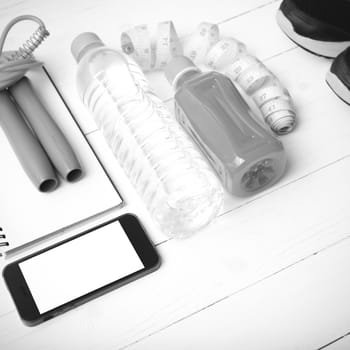 fitness equipment:running shoes,jumping rope,notepad,phone,water,juice and measuring tape on white wood background black and white color