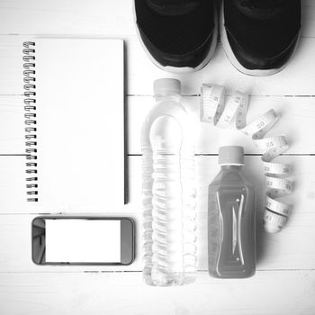 fitness equipment:running shoes,water,measuring tape,notepad,phone and juice on white wood background black and white color