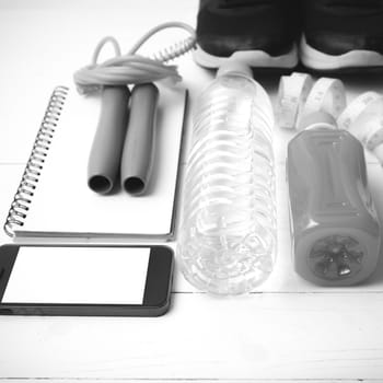 fitness equipment:running shoes,jumping rope,notepad,phone,water,juice and measuring tape on white wood background black and white color