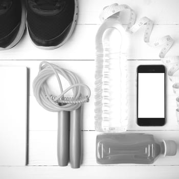 fitness equipment:running shoes,jumping rope,notepad,phone,water,juice and measuring tape on white wood background black and white color