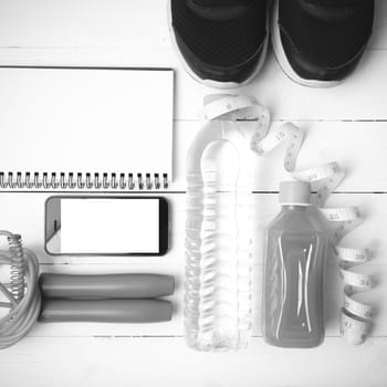 fitness equipment:running shoes,jumping rope,notepad,phone,water,juice and measuring tape on white wood background black and white color