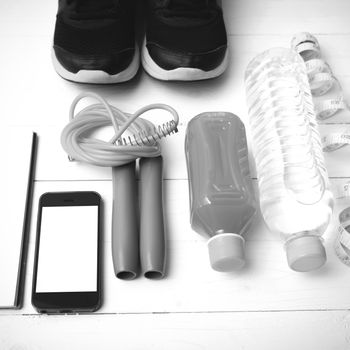 fitness equipment:running shoes,jumping rope,notepad,phone,water,juice and measuring tape on white wood background black and white color