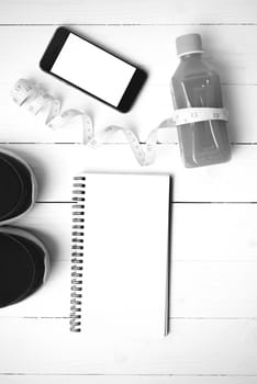 fitness equipment:running shoes,juice,measuring tape,notepad and phone on white wood background black and white color