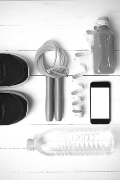 fitness equipment:running shoes,phone,measuring tape,water,juice and jumpong rope on white wood background black and white color